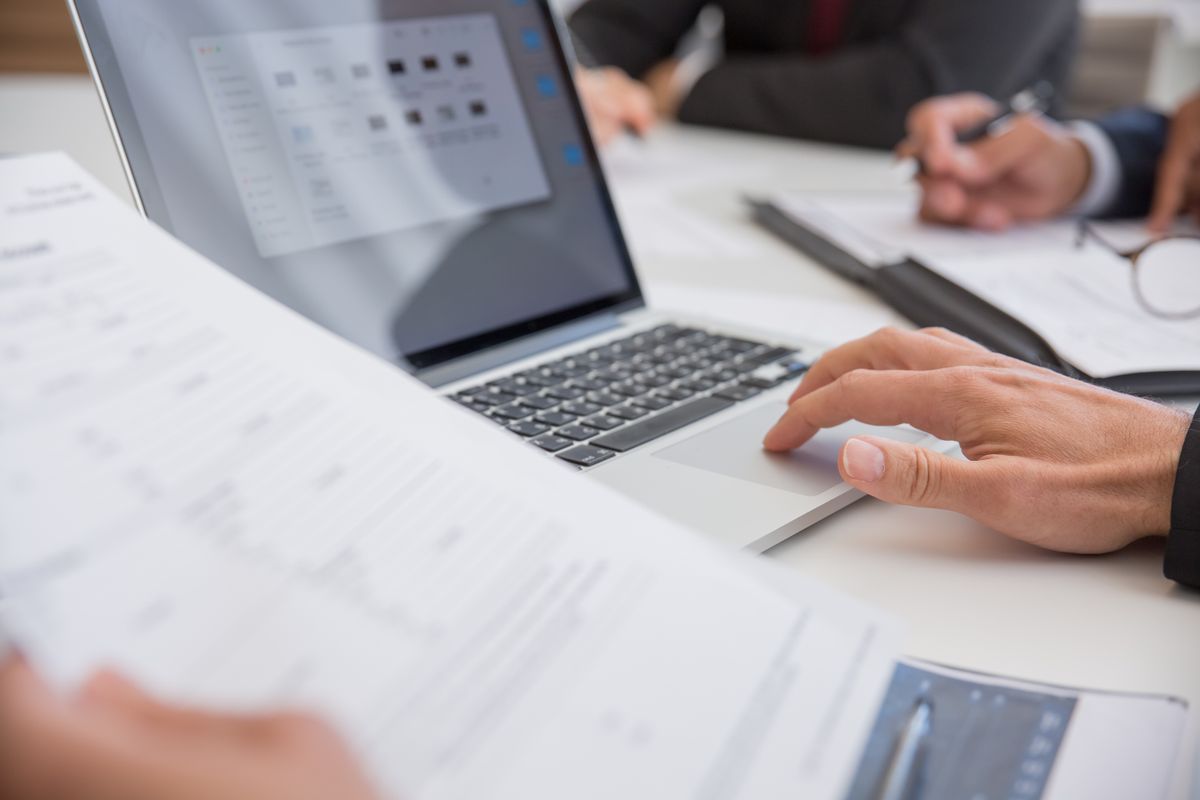 Hands reviewing planning documents and data on a laptop